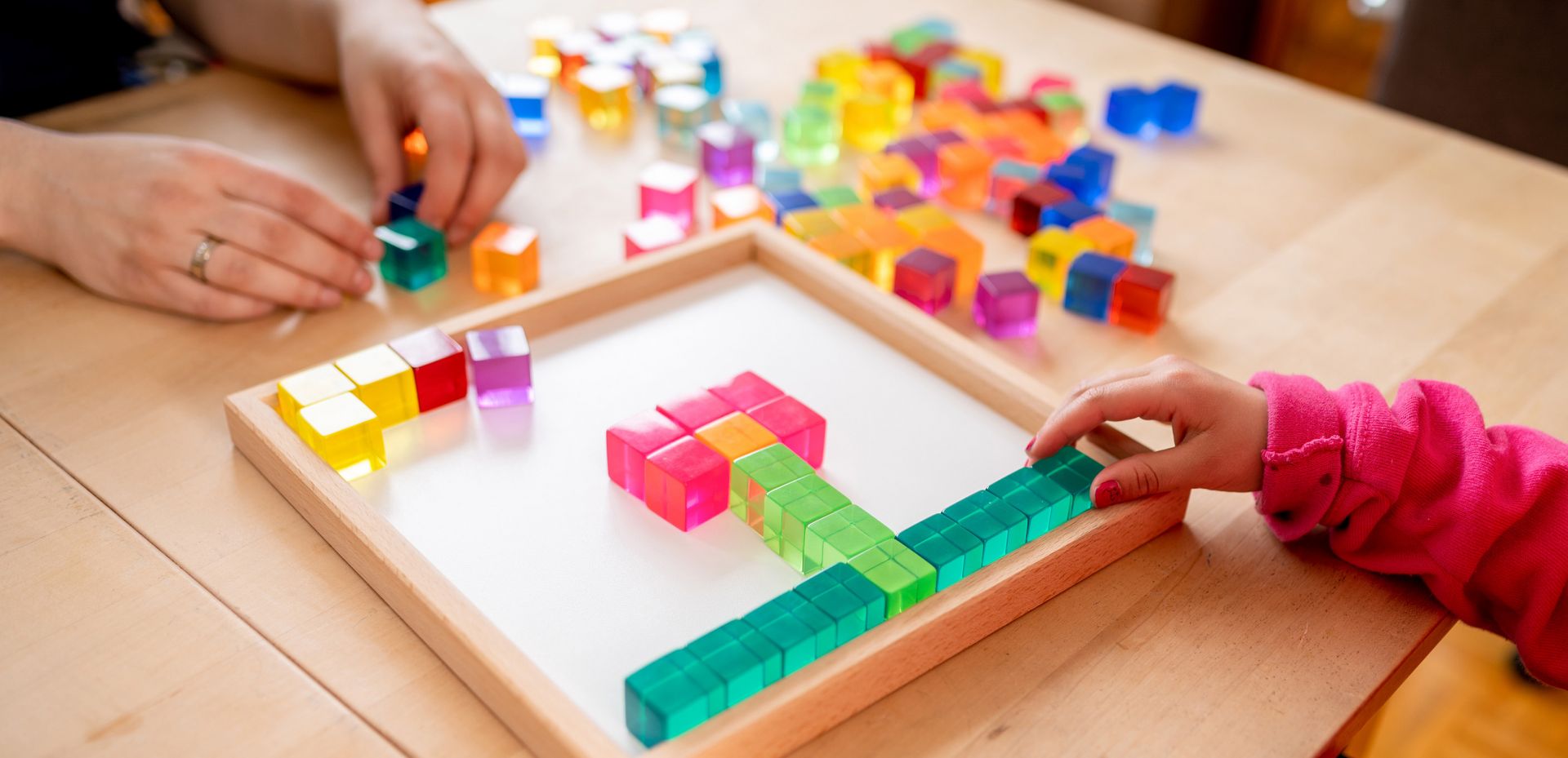 Foto einer Kinderhand, welche mit Spielzeugsteinen ein Muster legt.